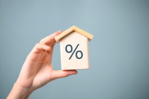 Hand holding a house-shaped block with a percentage symbol, representing interest rates