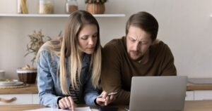 A couple going through paperwork with a laptop at a kitchen table